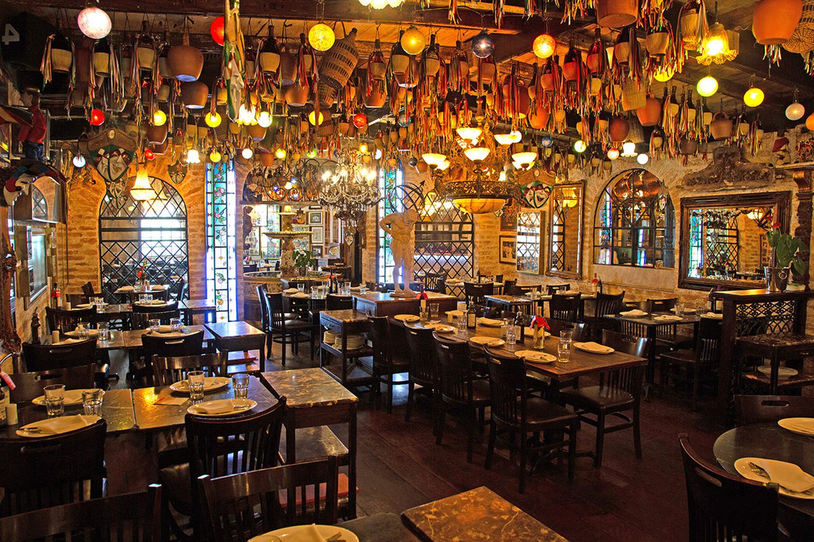 Salão principal da trattoria com panelas de cobre penduradas, arcos de pedra e vitrais