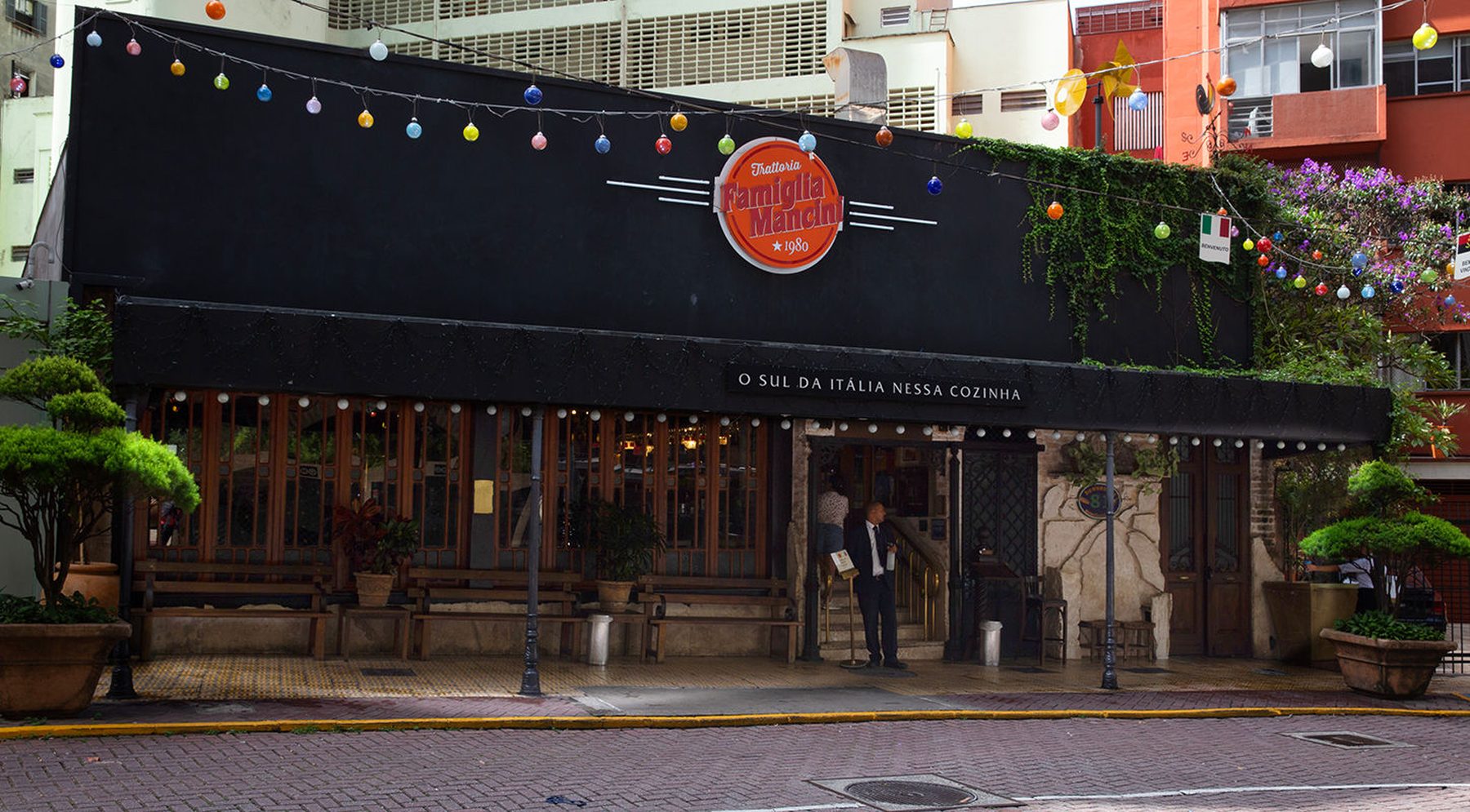 Fachada da Trattoria Famiglia Mancini à noite, com a placa redonda de 1980 e o letreiro O Sul da Itália nessa cozinha